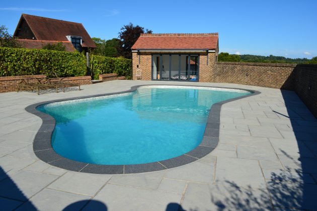 Free form shaped pool coping made to measure with bullnosed edge with contrasting pool terrace paving by cranbourne stone ltd